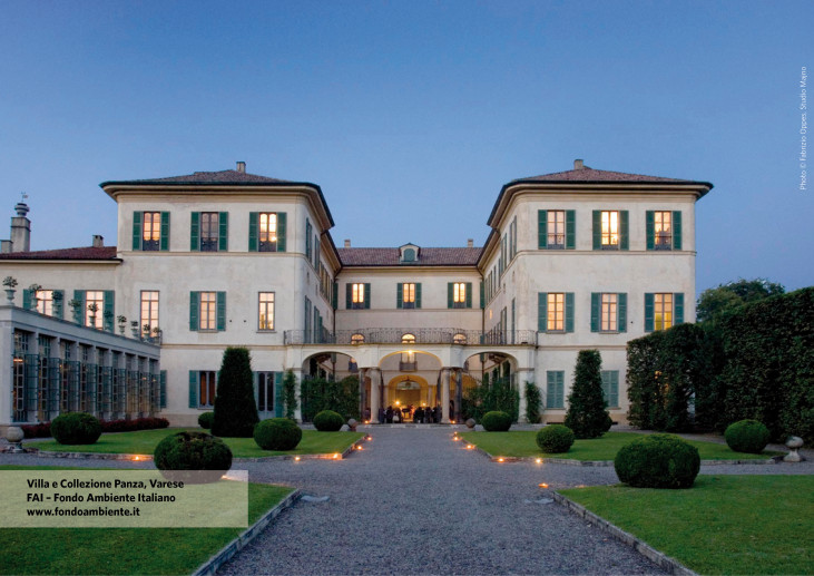 Fotografia frontale di Villa Panza a Varese al tramonto. La facciata elegante della villa, con persiane verdi e grandi finestre, è incorniciata da un giardino curato e un sentiero centrale in pietra che conduce all'ingresso. L'atmosfera è serena e l'illuminazione soffusa crea un senso di calore e accoglienza.