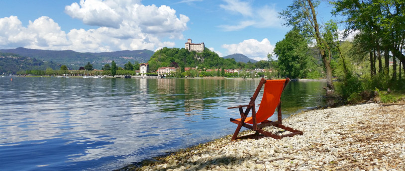 Lungolago di Aagera, con una spiaggetta. In riva al lago c'è una sdraio vuota e si vede la Rocca in lontananza.