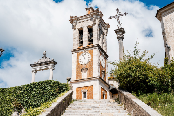 Scalinata che conduce alla torre campanaria del Sacro Monte di Varese, con cielo azzurro e vegetazione circostante.